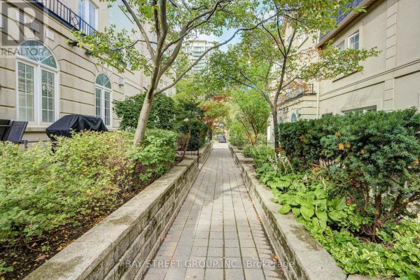 Stone pathway lined with green bushes and trees leading between townhouses. - 105 - 11 Everson Drive, Toronto