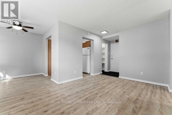 View of the living room, dining area, and hallway entrance with light wood floors and neutral walls. - 105 - 2044 Arrowsmith Drive, Ottawa