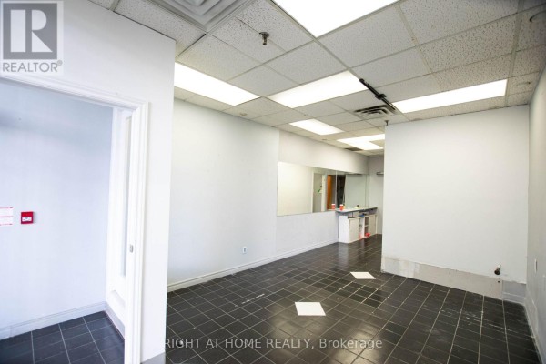 Empty commercial space with black tiled floor, white walls, drop ceiling, and mirrored wall section. - 105 - 2347 Kennedy Road, Toronto