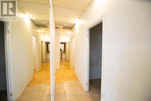 Interior hallway with tiled and wood-patterned flooring, white walls, and multiple doors. - 105 - 2347 Kennedy Road, Toronto