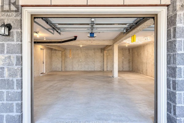 Empty, unfinished concrete garage interior with exposed pipes and ceiling lights. - 105 - 2540 William Jackson Drive, Pickering