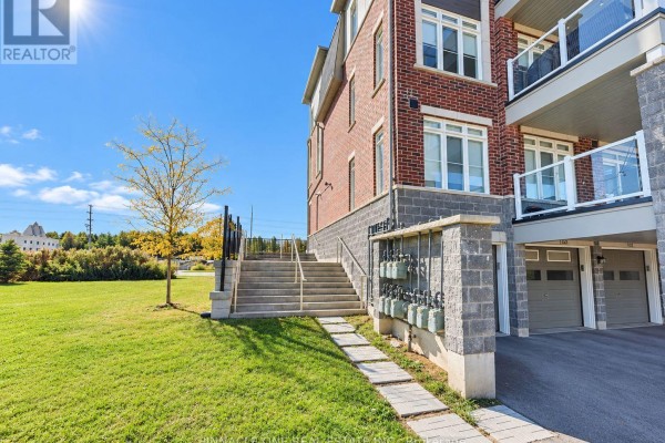Side view of a townhouse with a grassy lawn, concrete stairs, and gas meters on a block pillar. - 105 - 2540 William Jackson Drive, Pickering