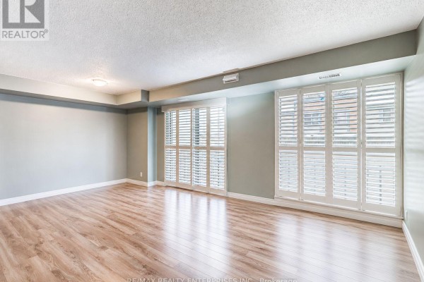 Empty living room with light wood floors and large white shuttered windows. - 105 - 3267 King Street E, Kitchener