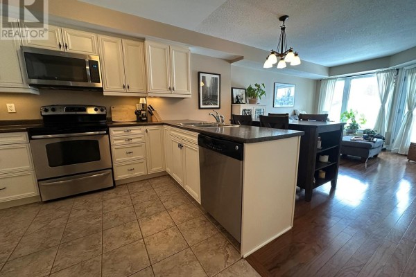 Open kitchen with stainless steel appliances, granite countertops, and adjacent dining area. - 105 - 398 Van Buren Street, North Grenville