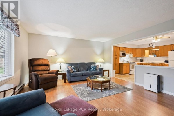 Living room with blue sofa, recliner, and view into kitchen with wood cabinets. - 105 - 497 Birmingham Street W, Wellington North