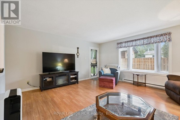 Living room with large TV, electric fireplace, blue sofa, ottoman, and large window. - 105 - 497 Birmingham Street W, Wellington North