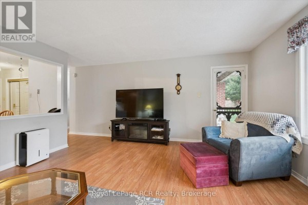 Living room with TV, blue sofa, ottoman, doorway, and view into hallway. - 105 - 497 Birmingham Street W, Wellington North