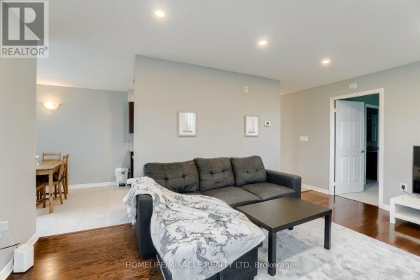 Living room showing sofa, coffee table, and access to dining area and bathroom. - 105 - 55 Via Rosedale Road, Brampton