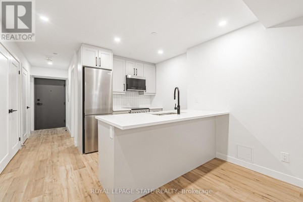 Modern kitchen with white cabinetry, stainless steel appliances, and a grey island with a black faucet. - 105 - 555 Sanatorium Road, Hamilton
