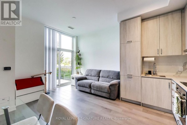 Living area with a grey sofa, glass sliding door to balcony, and floor-to-ceiling window. - 105 - 60 Honeycrisp Crescent, Vaughan