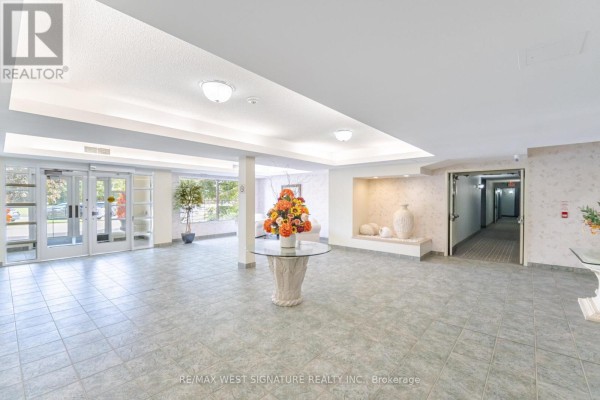 A spacious apartment building lobby with beige floor tiles and a large floral arrangement. - 105 - 75 Treelawn Boulevard, Vaughan
