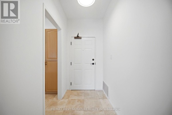 An interior hallway with beige tile flooring leading to a white front door. - 105 - 75 Treelawn Boulevard, Vaughan