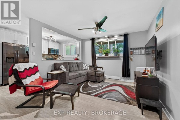 Living room with grey sectional sofa, armchair, coffee table, and an open view to the kitchen. - 105 - 835 Milford Drive, Kingston