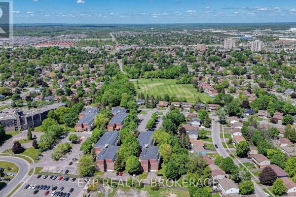 Aerial view of apartment buildings surrounded by houses, streets, and green spaces under a blue sky. - 105 - 835 Milford Drive, Kingston