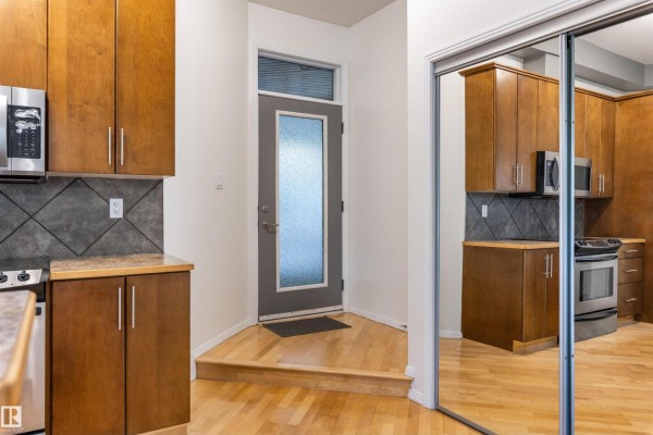 View of a compact kitchen with wood cabinets, stainless steel appliances, and a glass-paned door. - #105 10531 117 St Nw, Edmonton