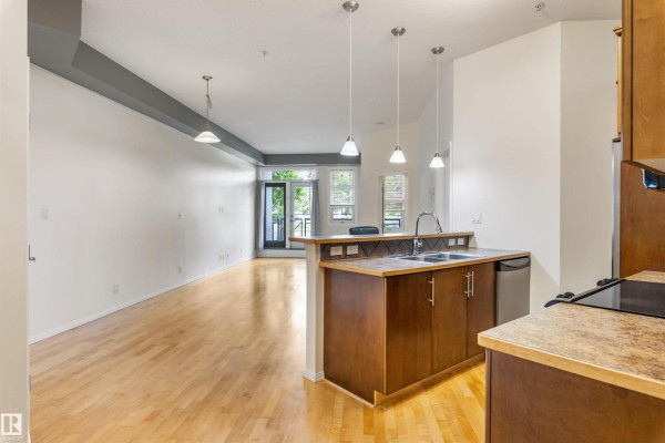 Open-concept living area and kitchen with hardwood floors, a kitchen island, and large windows. - #105 10531 117 St Nw, Edmonton