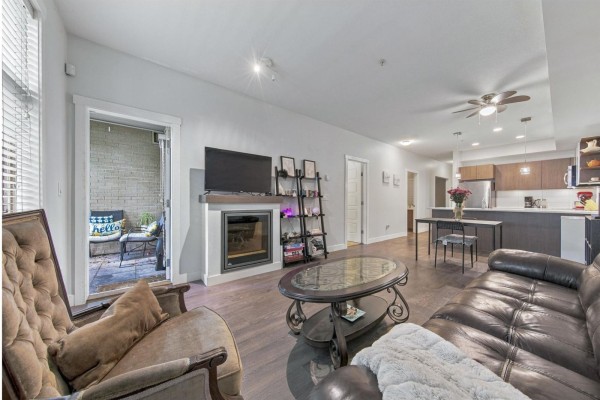 Living room with fireplace, brown leather sofa, armchair, coffee table, and access to patio. - 105 19936 56 Avenue, Langley