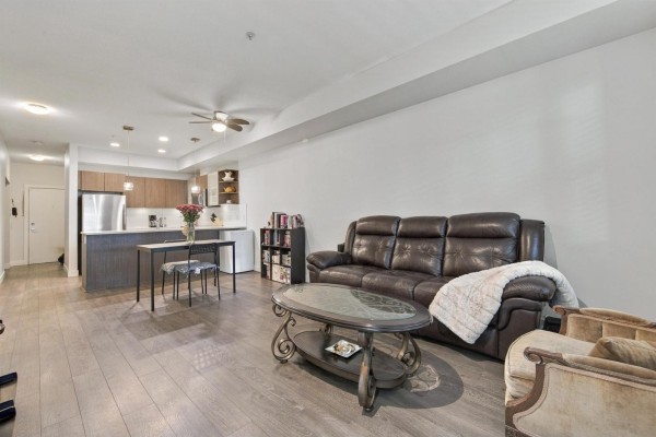 Spacious living area with dark leather sofa, armchair, coffee table, and view of the kitchen. - 105 19936 56 Avenue, Langley