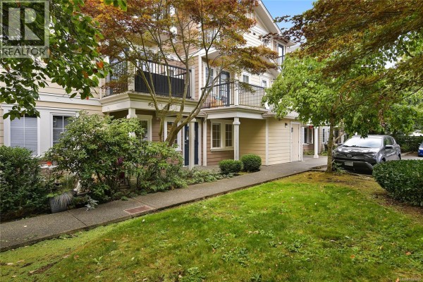 Apartment building with balconies, brown and beige siding, and a nearby car. - 105 2695 Deville Rd, Langford