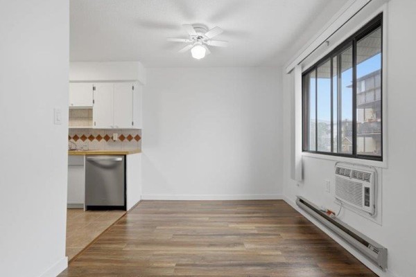 Empty dining area with hardwood floors and a large window showing a building view. - 105 32033 Old Yale Road, Abbotsford