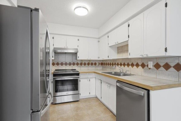 Kitchen with white cabinets, stainless steel appliances including a refrigerator, stove, and dishwasher. - 105 32033 Old Yale Road, Abbotsford
