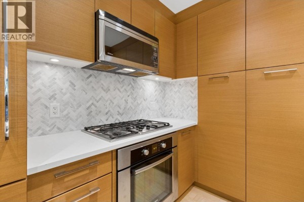 Close-up of gas stovetop and oven with herringbone tile backsplash and wood cabinetry. - 105 5868 Agronomy Road, Vancouver