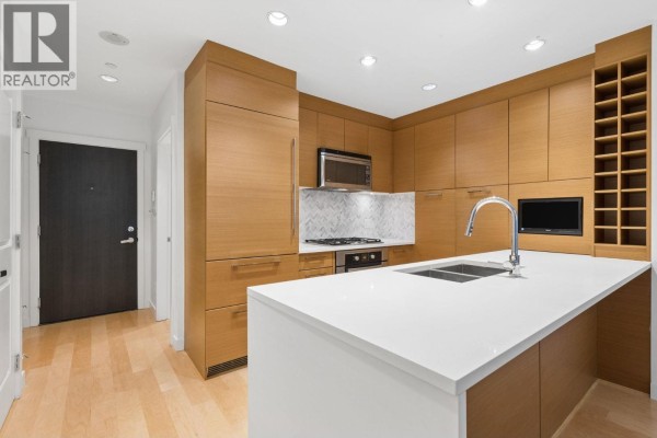 Kitchen with island, wood cabinetry, stainless steel appliances, and entryway hallway. - 105 5868 Agronomy Road, Vancouver