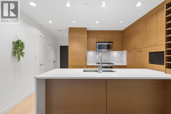 Spacious kitchen with island, white countertops, wood cabinets, and view of hallway and doors. - 105 5868 Agronomy Road, Vancouver