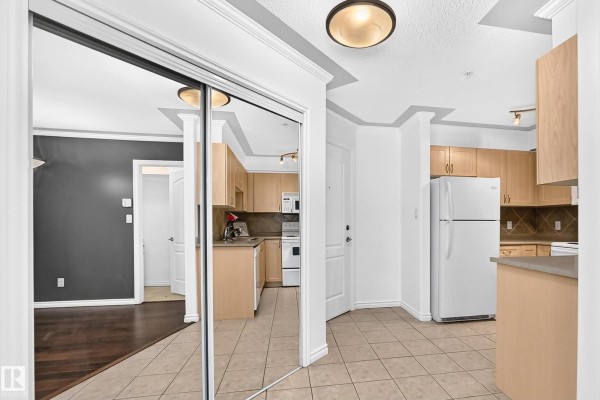Apartment hallway with tiled floor, mirrored closet, and view into kitchen. - #105 9938 104 St Nw, Edmonton