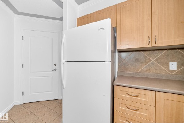 Kitchenette with light wood cabinets, beige countertop, white refrigerator, and tiled backsplash. - #105 9938 104 St Nw, Edmonton