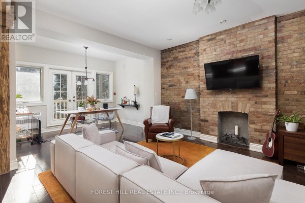 Living room with white sectional sofa, exposed brick wall, and French doors leading outside. - 105 Balmoral Avenue, Toronto