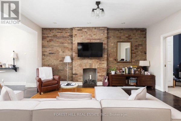 Living room facing a brick fireplace, wooden entertainment unit, and entryway to another room. - 105 Balmoral Avenue, Toronto