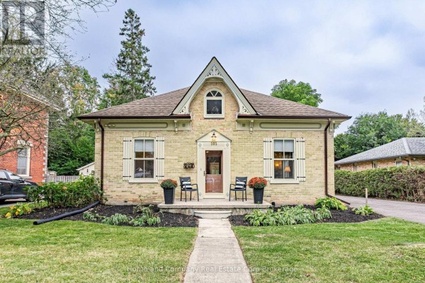 Front view of a light yellow brick house with white shutters and a covered porch with two chairs. - 105 Centre Street, Stratford