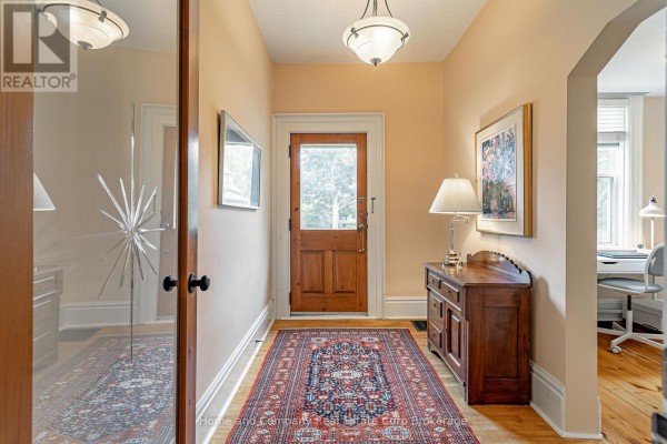 Interior entryway with a wooden front door, patterned rug, and a dark wood cabinet. - 105 Centre Street, Stratford