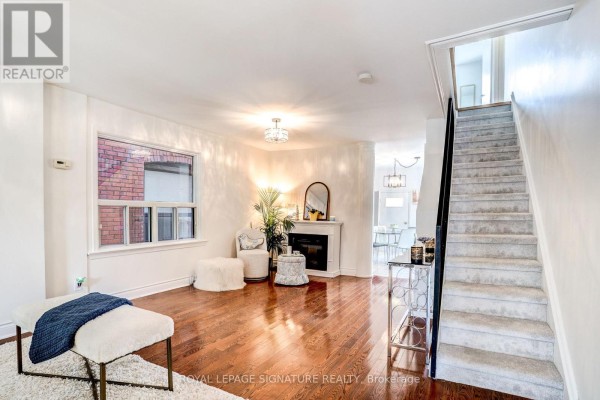 Living room with hardwood floors, white walls, fireplace, and stairs. - 105 Earlscourt Avenue, Toronto