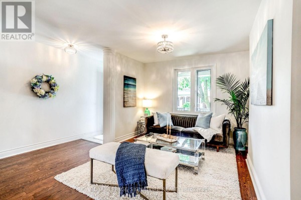 Living room with dark sofa, glass coffee table, plush rug, and large window. - 105 Earlscourt Avenue, Toronto