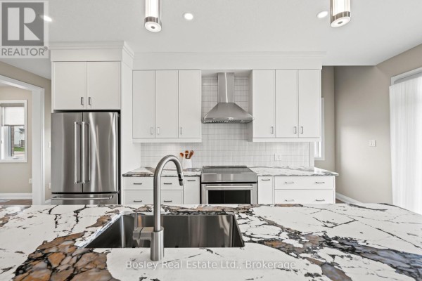 Kitchen island with a marble countertop and sink, facing white cabinets and stainless steel appliances. - 105 Haylock Avenue, Centre Wellington