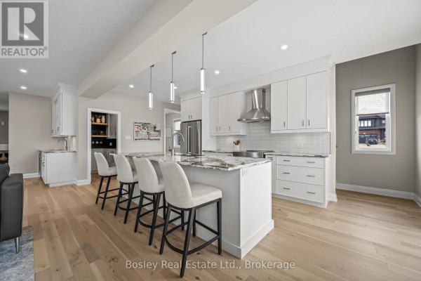 Kitchen island with pendant lights, bar stools, and white cabinets, adjacent to the living area. - 105 Haylock Avenue, Centre Wellington