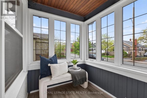 Sunroom entrance with a wooden door, patterned rug, white armchair, grey side table, and ornate light fixture. - 105 Highland Avenue, St  Catharines