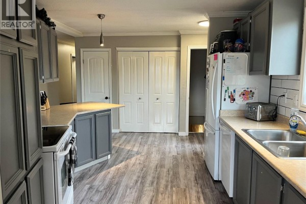 Kitchen with grey cabinets, a peninsula, laminate flooring, and double white doors. - 105 Jasper Drive, Logan Lake