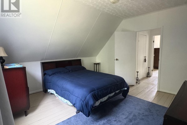 Bedroom with a navy blue comforter on a queen bed, sloped ceiling, and light wood floors. - 105 Wilkes Cove Road, Middle Lahave