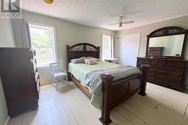Bedroom with a dark wood bed frame, green bedding, white chair, dresser, and wood floors. - 105 Wilkes Cove Road, Middle Lahave