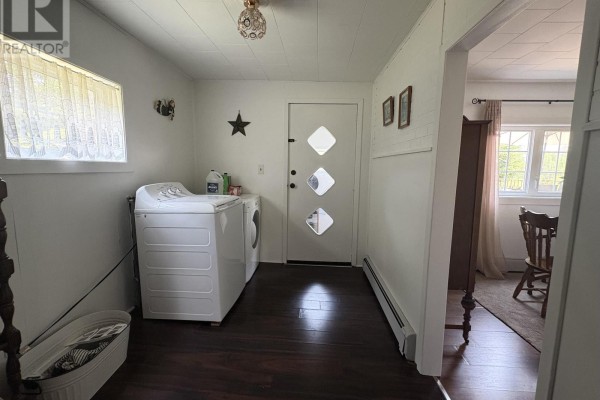 Laundry room with white washer and dryer, dark wood-look floor, white paneled walls, and a diamond-patterned door. - 105 Wilkes Cove Road, Middle Lahave