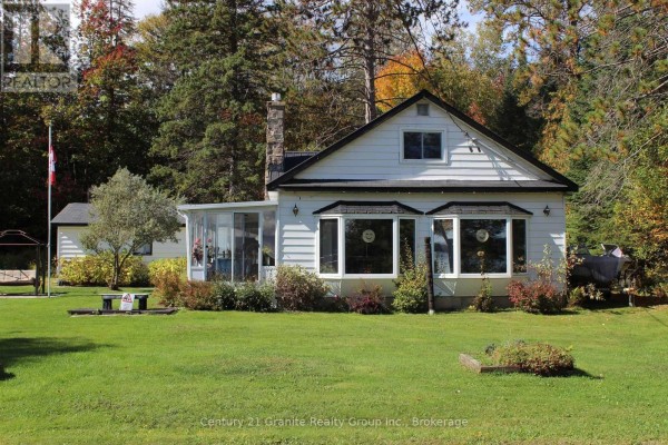 Side view of white cottage with bay windows and sunroom addition. - 1051 Halls Lake Road, Algonquin Highlands