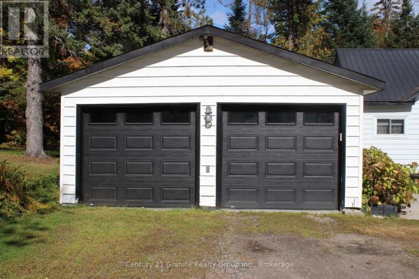 White detached garage with two black garage doors. - 1051 Halls Lake Road, Algonquin Highlands