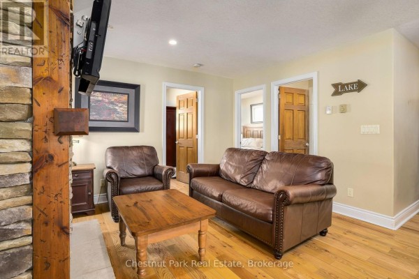 Living room with leather seating, stone fireplace, and two doorways leading to other rooms. - 1052 Rat Bay 103-1 Road, Lake Of Bays