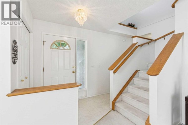 Interior view of a white entryway with a glass front door, a coat closet, and a carpeted staircase. - 10521 Hidden Valley Drive Nw, Calgary