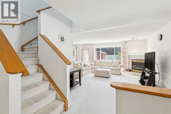 View of a living room with a white carpet, a fireplace, and a staircase leading to a second floor. - 10521 Hidden Valley Drive Nw, Calgary