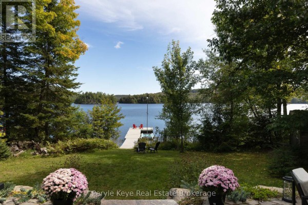 A grassy yard with two potted plants leads to a dock on a wide blue lake. - 1054 Inawendawin Road, Lake Of Bays