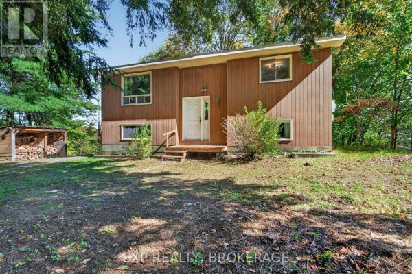 A slightly angled front view of the house showing the porch and a wood shed. - 1054 York Road, Frontenac